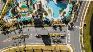 An aerial view of a resort with a central pool, multiple swimming pools, and a road with a pedestrian crossing.