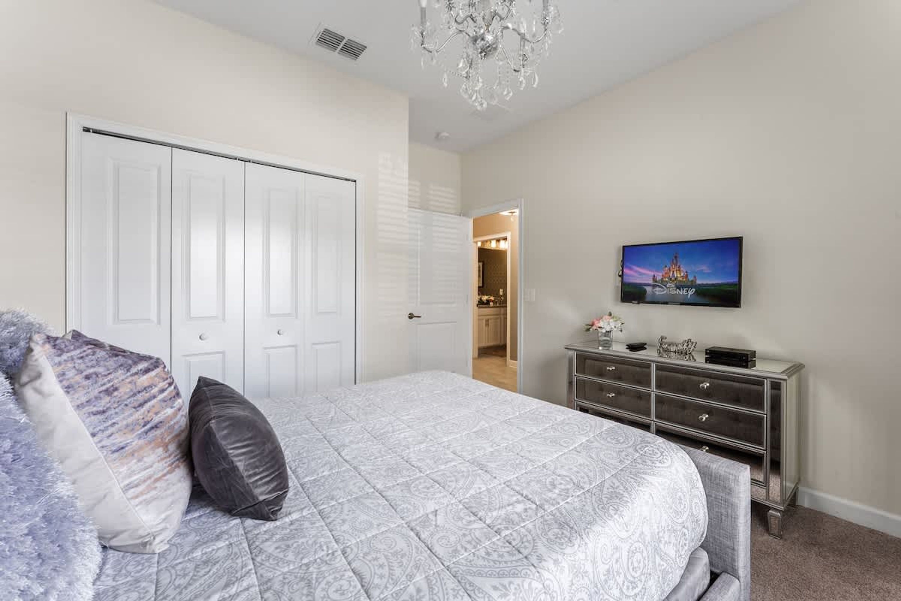 A bedroom with a bed, a dresser, a television, and a door leading to a bathroom.