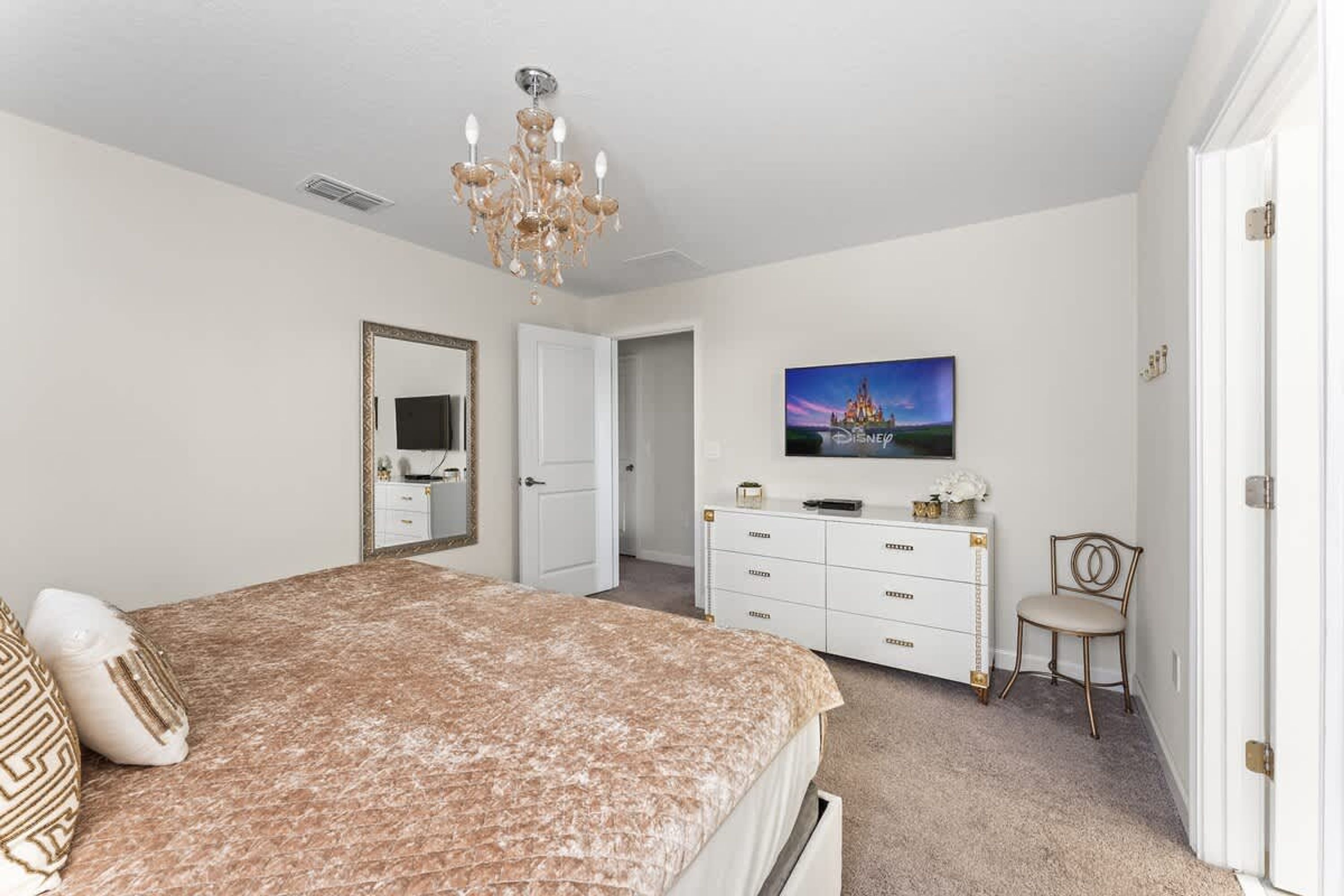 A bedroom with a bed, dresser, chair, and a TV on the wall.