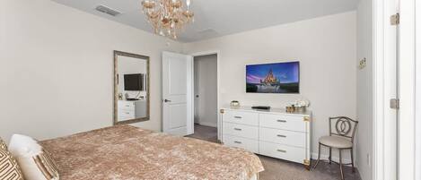 A bedroom with a bed, dresser, chair, and a TV on the wall.