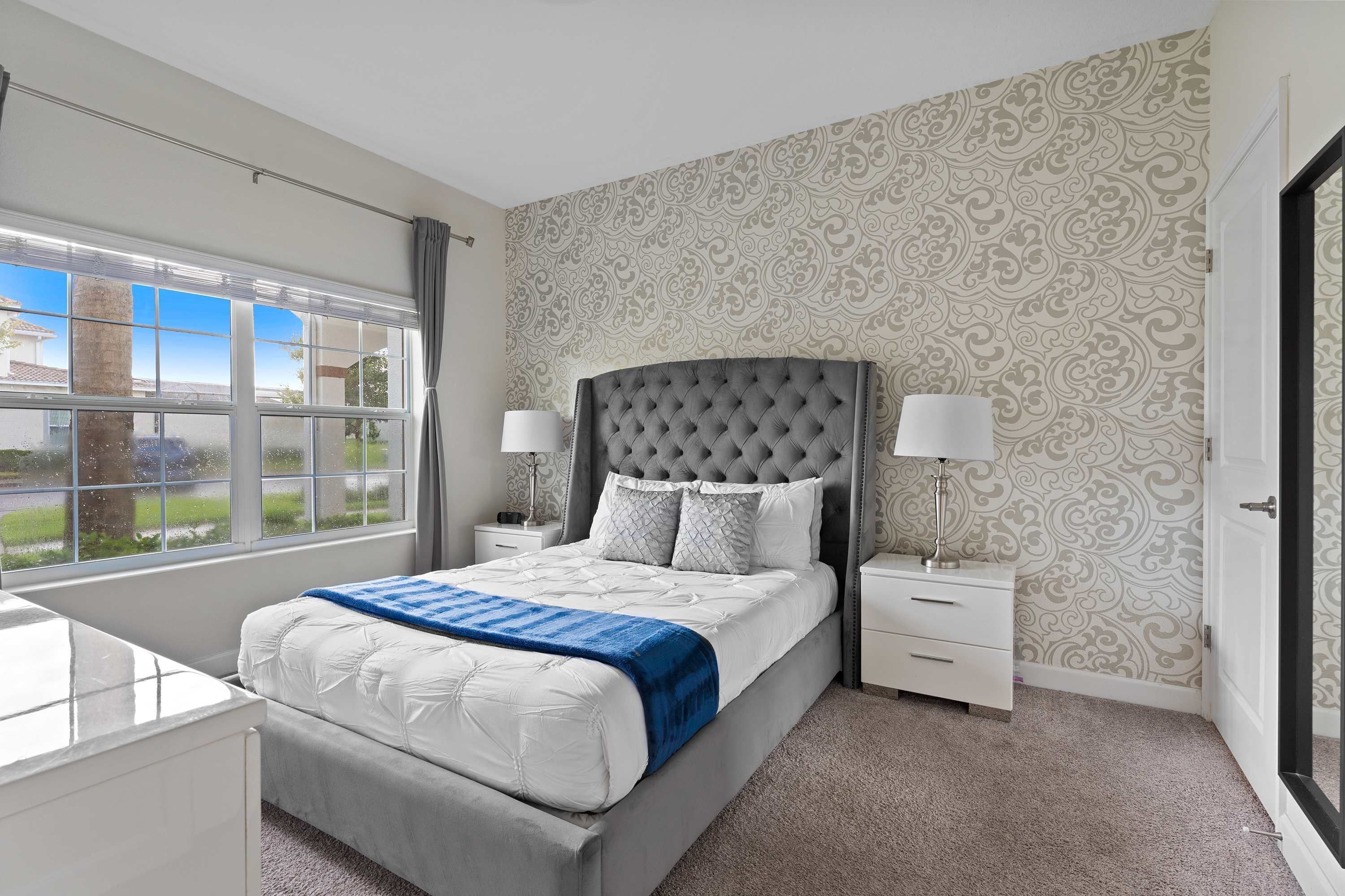 A bedroom with a large bed, two bedside tables, a window, and patterned wallpaper.