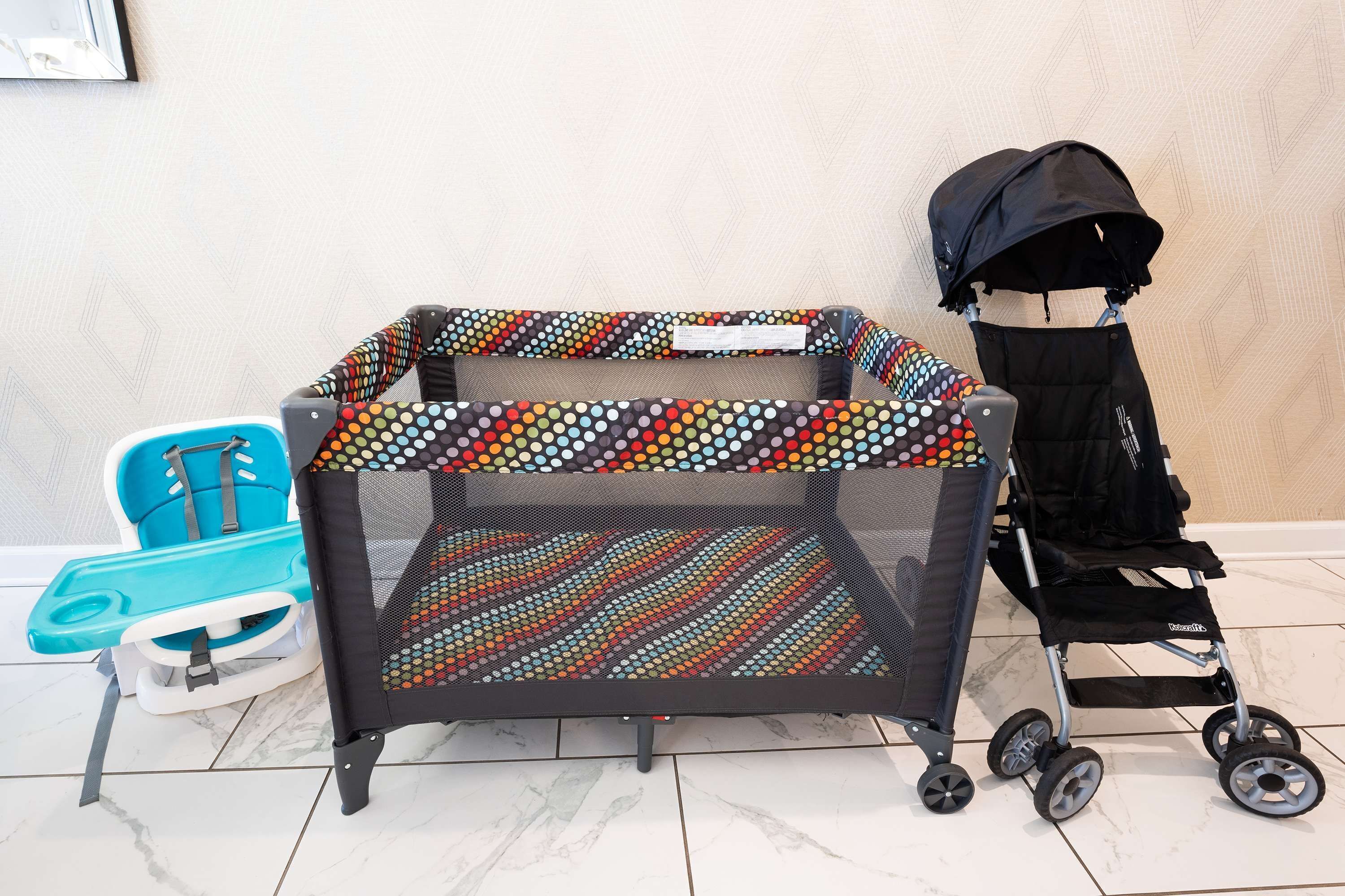 A baby play area with a colorful playpen, a blue baby seat, and a black stroller.
