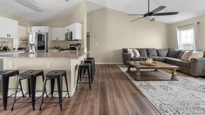 Une cuisine moderne dotée d’un îlot central, de tabourets de bar, d’un coin repas avec un canapé et une table basse, et d’un ventilateur de plafond.