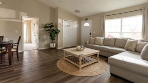 Un salon avec une table basse en bois, un canapé beige et un coin repas comprenant une table et des chaises.