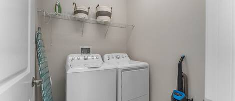 A laundry room with a washer and dryer, a shelf with laundry supplies, and a vacuum cleaner.