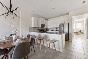 A modern kitchen with white cabinetry, a central island, and a dining area with a round table and chairs. - 3BR up to 8 People at Champions Gate (Davenport)