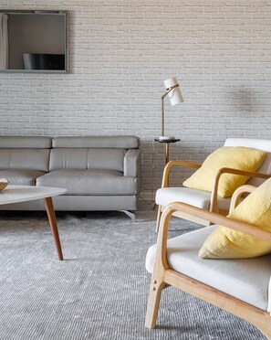 A modern living room with a grey sofa, a round coffee table, a wooden armchair with yellow cushions, and a floor lamp. - 3BR up to 8 People at Champions Gate (Davenport)