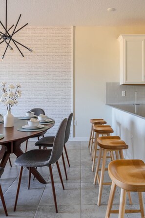 A modern dining area with a brick wall, a wooden dining table, and bar stools. - 3BR up to 8 People at Champions Gate (Davenport)