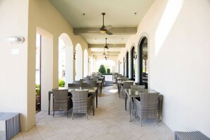 An outdoor patio with wicker tables and chairs, a ceiling fan, and a view of the street in the background. - 3BR up to 8 People at Champions Gate (Davenport)