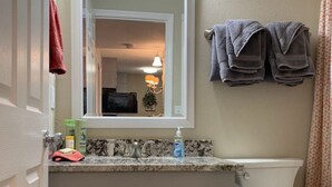 Un baño con inodoro blanco, un lavabo con espejo y un perchero con toallas.