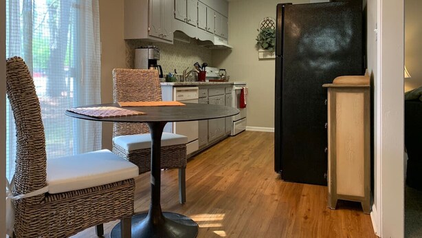 Una cocina compacta con comedor, que incluye una mesa redonda, sillas de mimbre, un refrigerador negro y suelo de madera.