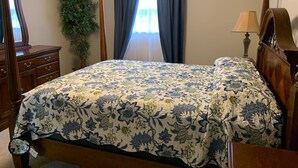 Un dormitorio con una cama con dosel, una mesita de noche, una lámpara, un aparador y una planta en maceta.
