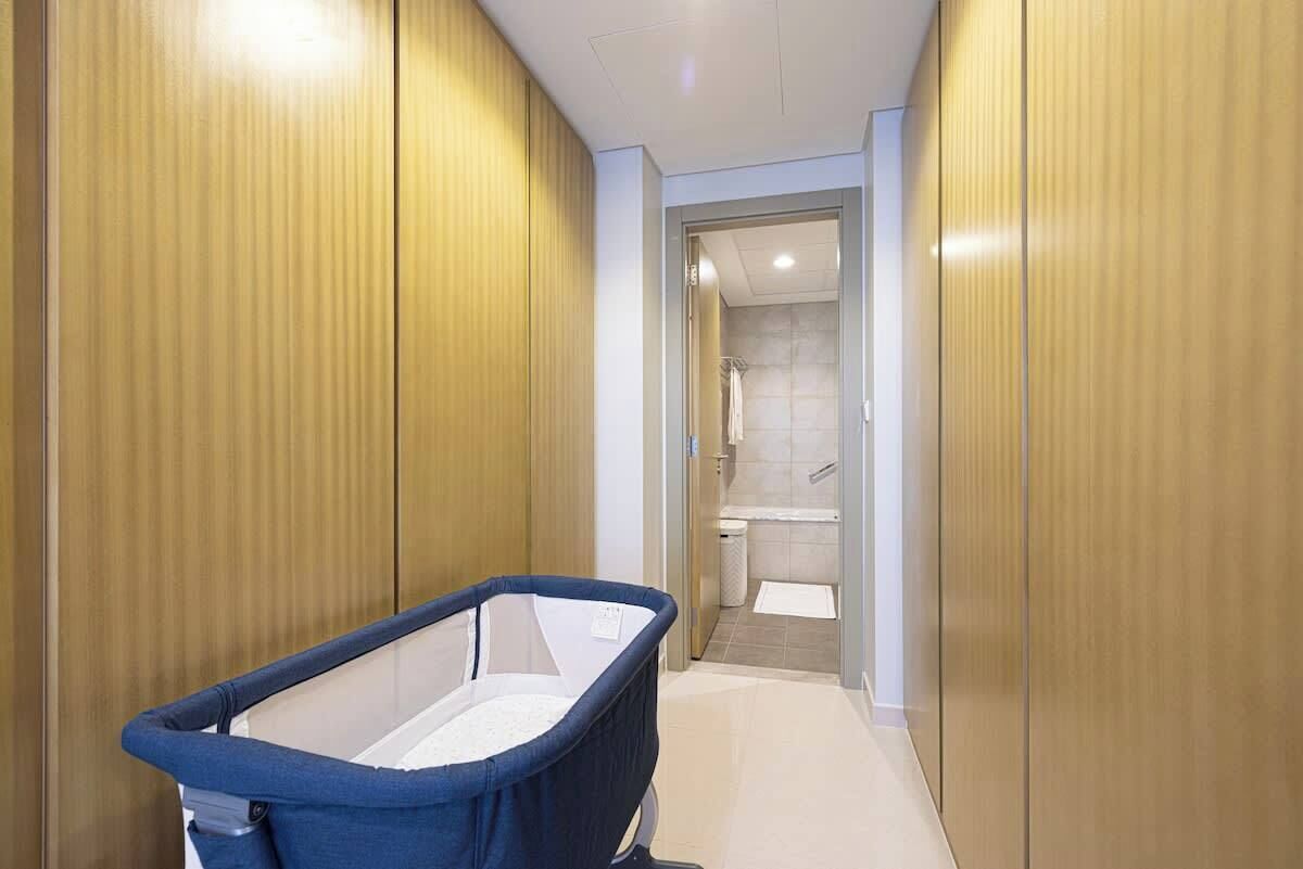 Un couloir étroit, avec une petite baignoire pour bébé bleue au premier plan et un espace douche à l’arrière-plan.