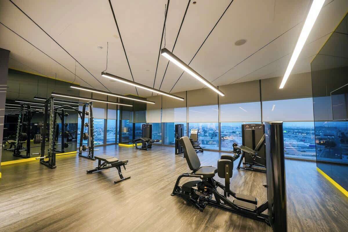 Ett modernt gym med olika typer av träningsutrustning, stora fönster och utsikt över staden.