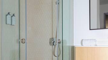 Een moderne badkamer met een douche met glazen wanden, een houten wastafelmeubel en een spiegel boven de wastafel.