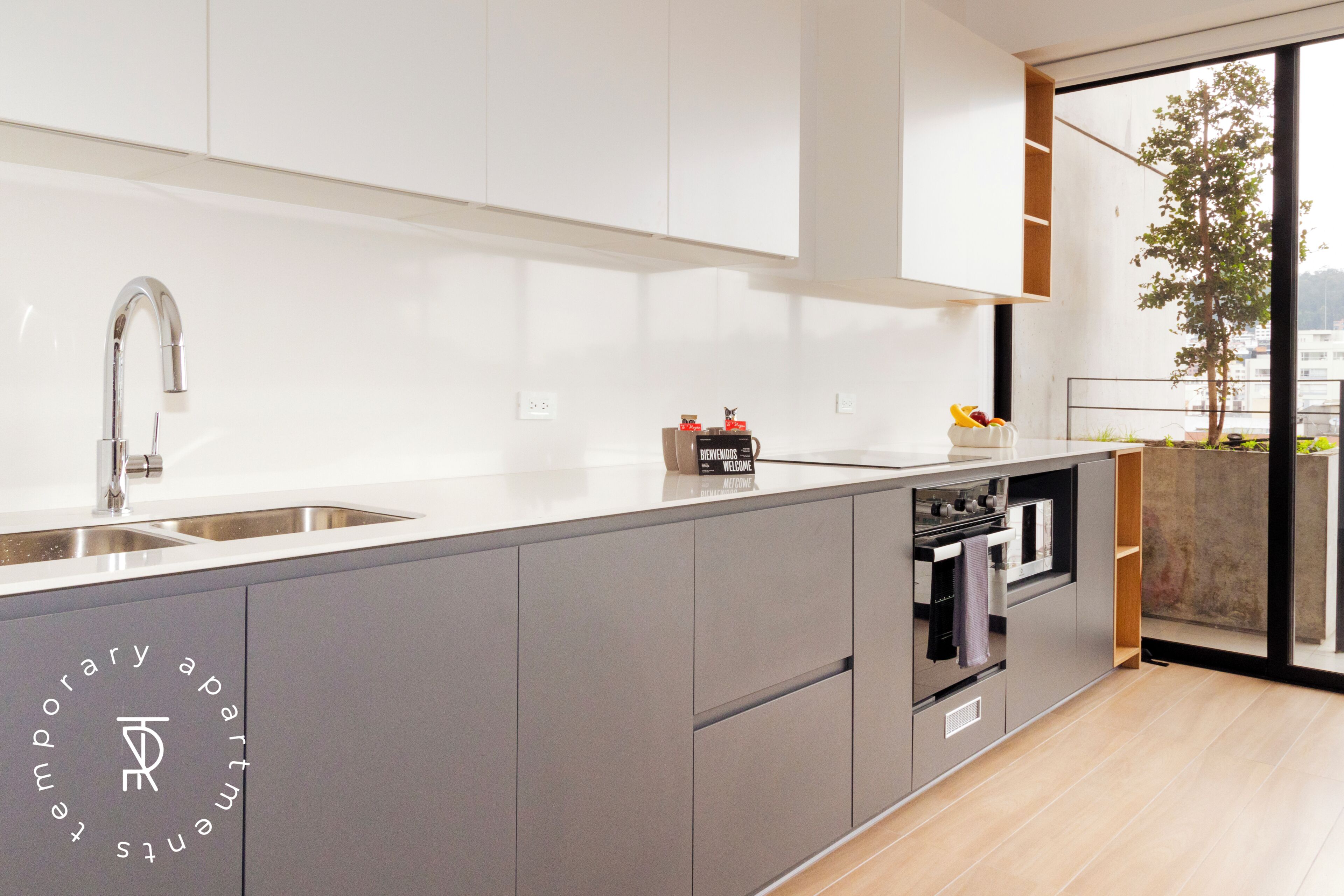 Una cucina moderna con forno integrato, un lavello e una finestra che dà su un balcone.