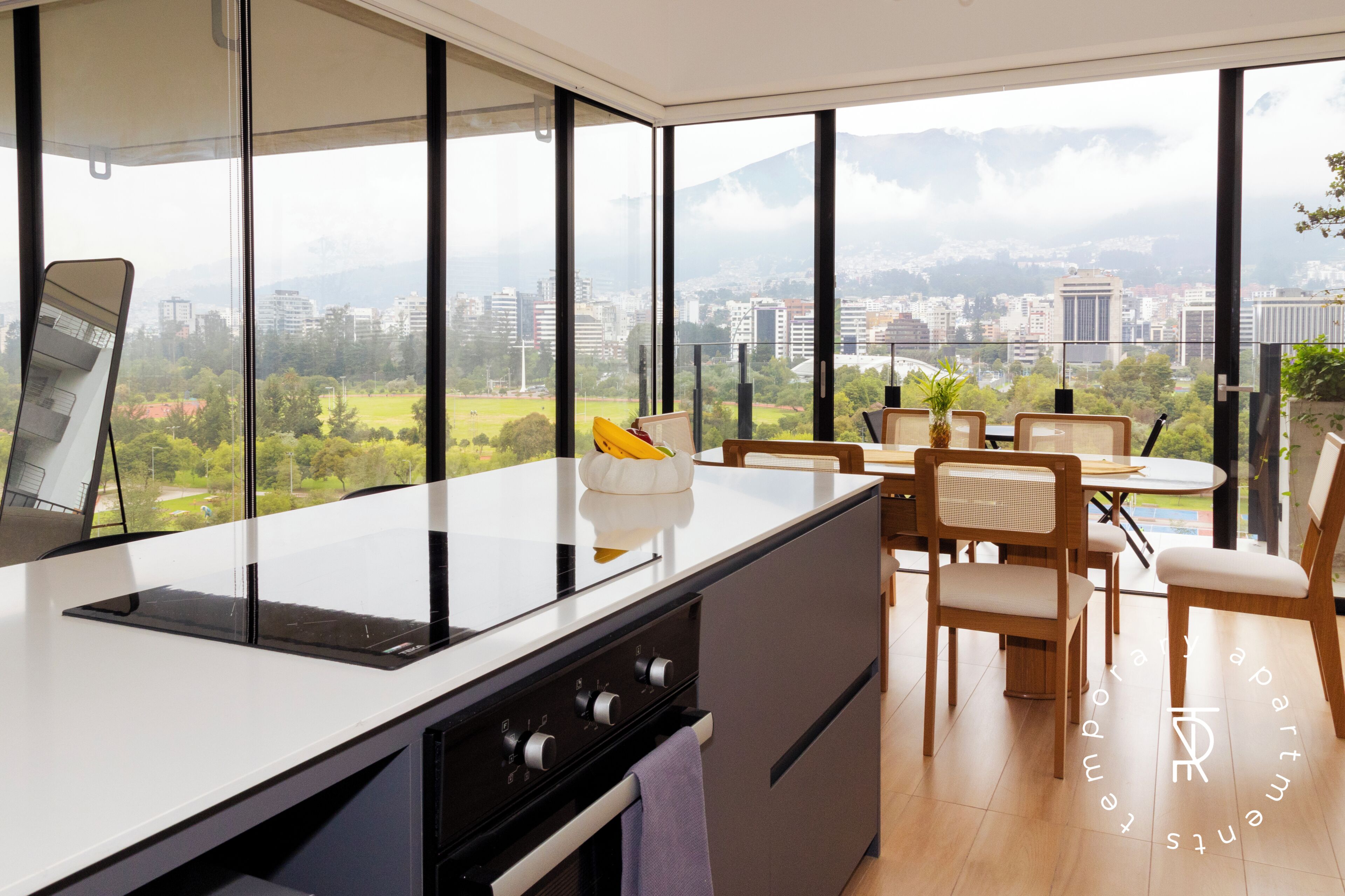 A modern kitchen with a large window, a dining area with a table and chairs, and a view of a cityscape.