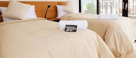Habitación de hotel con dos camas, cada una con colcha y almohadas color beige. Un cartel en la cama dice
