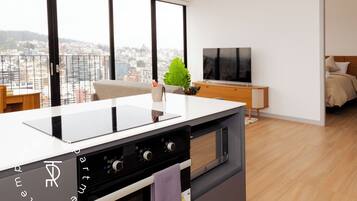 A modern kitchen with a built-in oven and stovetop, a large window with a city view, a wooden cabinet, and a flat-screen TV.