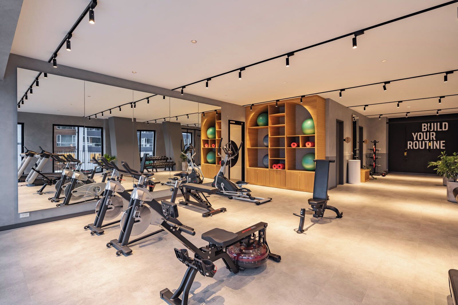 Un gimnasio moderno con diversos equipos de ejercicio, un espejo grande y un letrero motivacional.