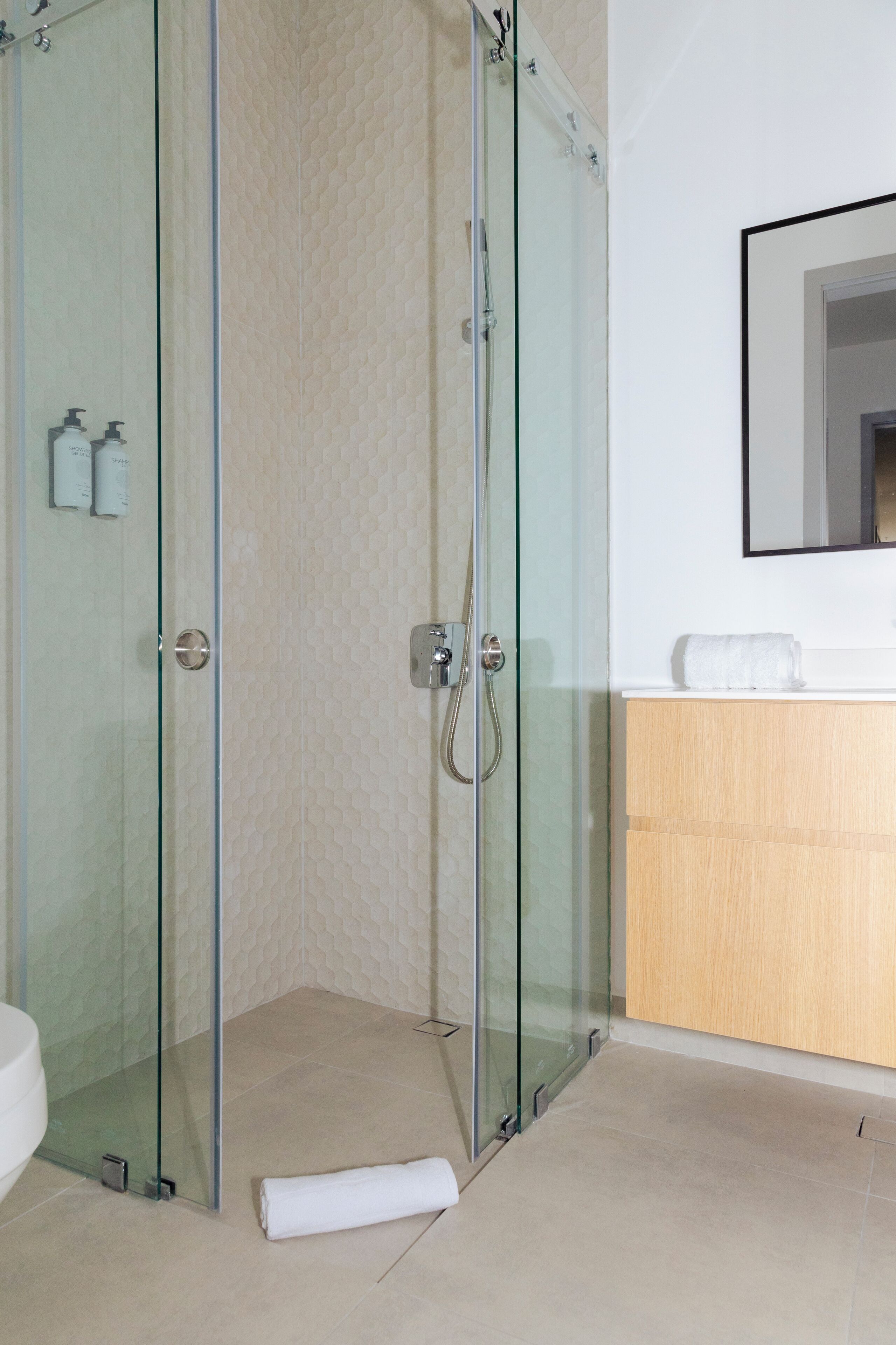 A modern bathroom with a glass-enclosed shower, a wooden vanity, and a white toilet.