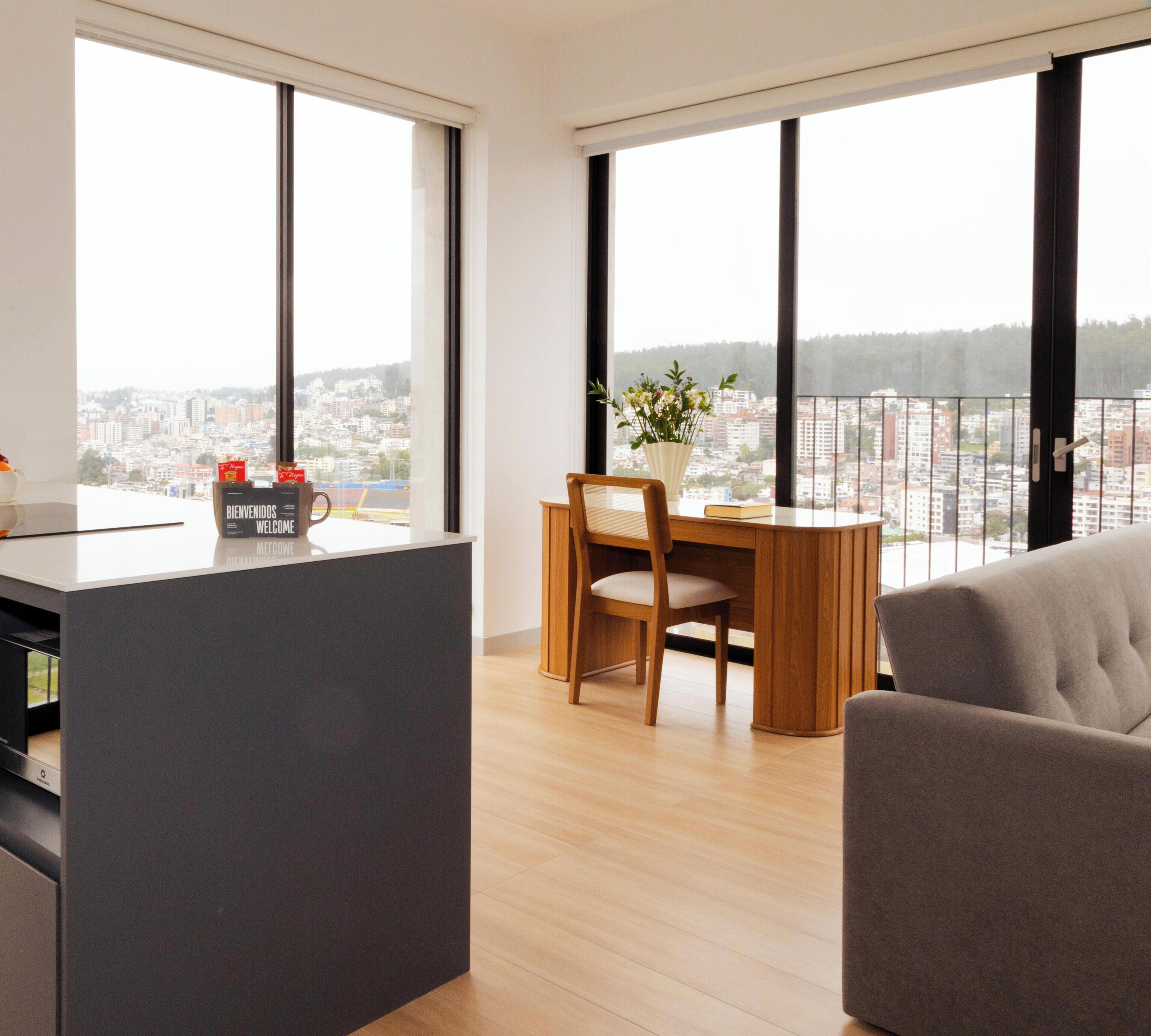 A modern living space with a dining area, a sofa, and a view of a cityscape through large windows.