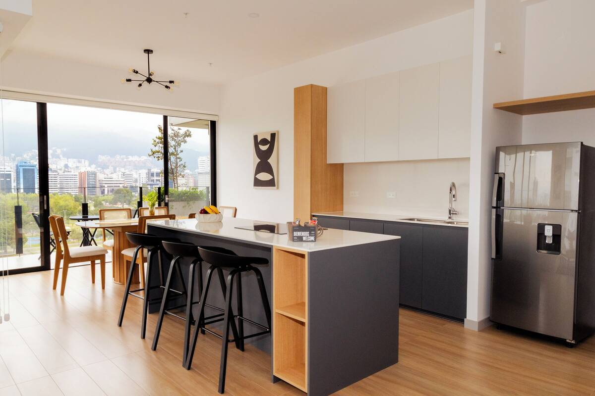 A modern kitchen with a large island, bar stools, and a stainless steel refrigerator.