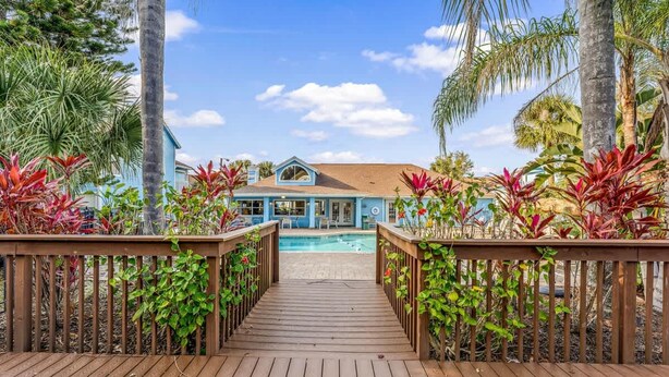 A wooden deck leading to a pool area with a house in the background.