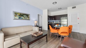 A living room with a sofa, coffee table, and orange chairs. There is a painting on the wall and a kitchen in the background. - Hotel Apt at Celebration 10 min From Disney (Celebration)