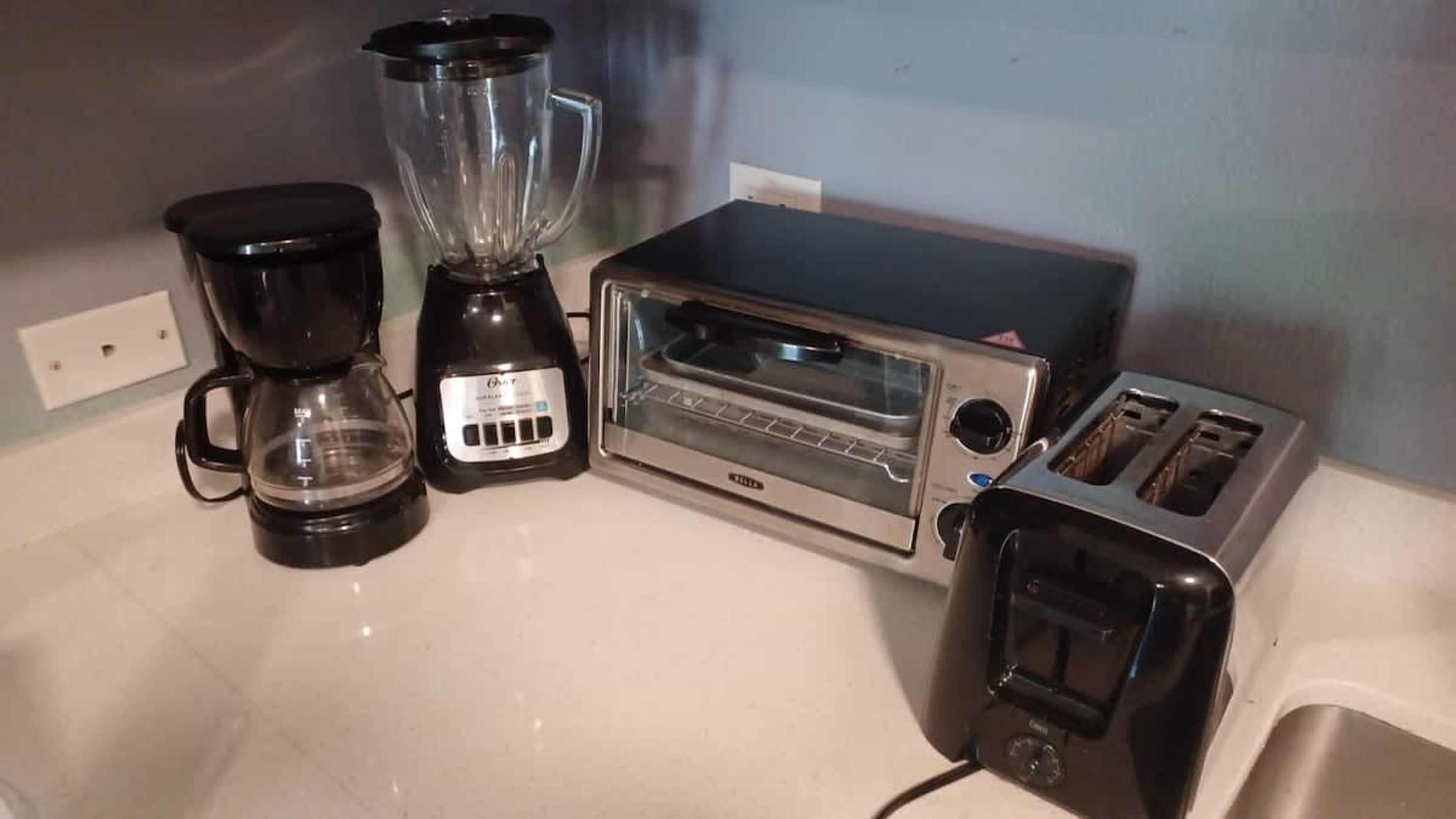 A kitchen with a coffee maker, a blender, a toaster oven, and a toaster.