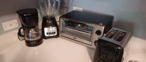 A kitchen with a coffee maker, a blender, a toaster oven, and a toaster.
