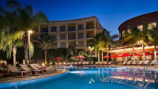 A swimming pool with lounge chairs and umbrellas, surrounded by palm trees and a building with multiple balconies. - Hotel Apt at Celebration 10 min From Disney (Celebration)