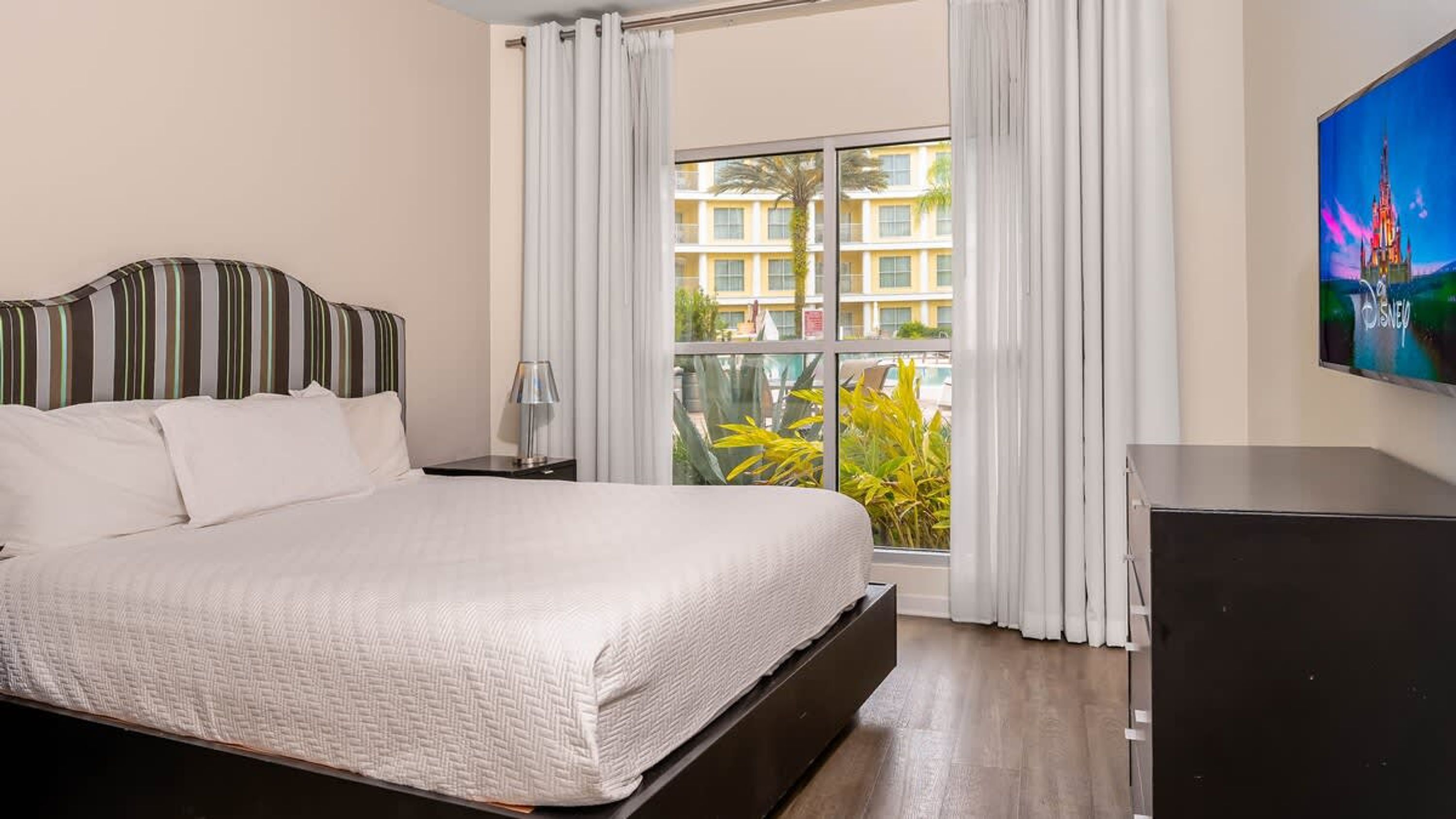Quarto de hotel com uma cama, televisão e janela com cortinas.