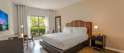 A hotel room with a large bed, a desk, a chair, a TV, and a window with curtains.