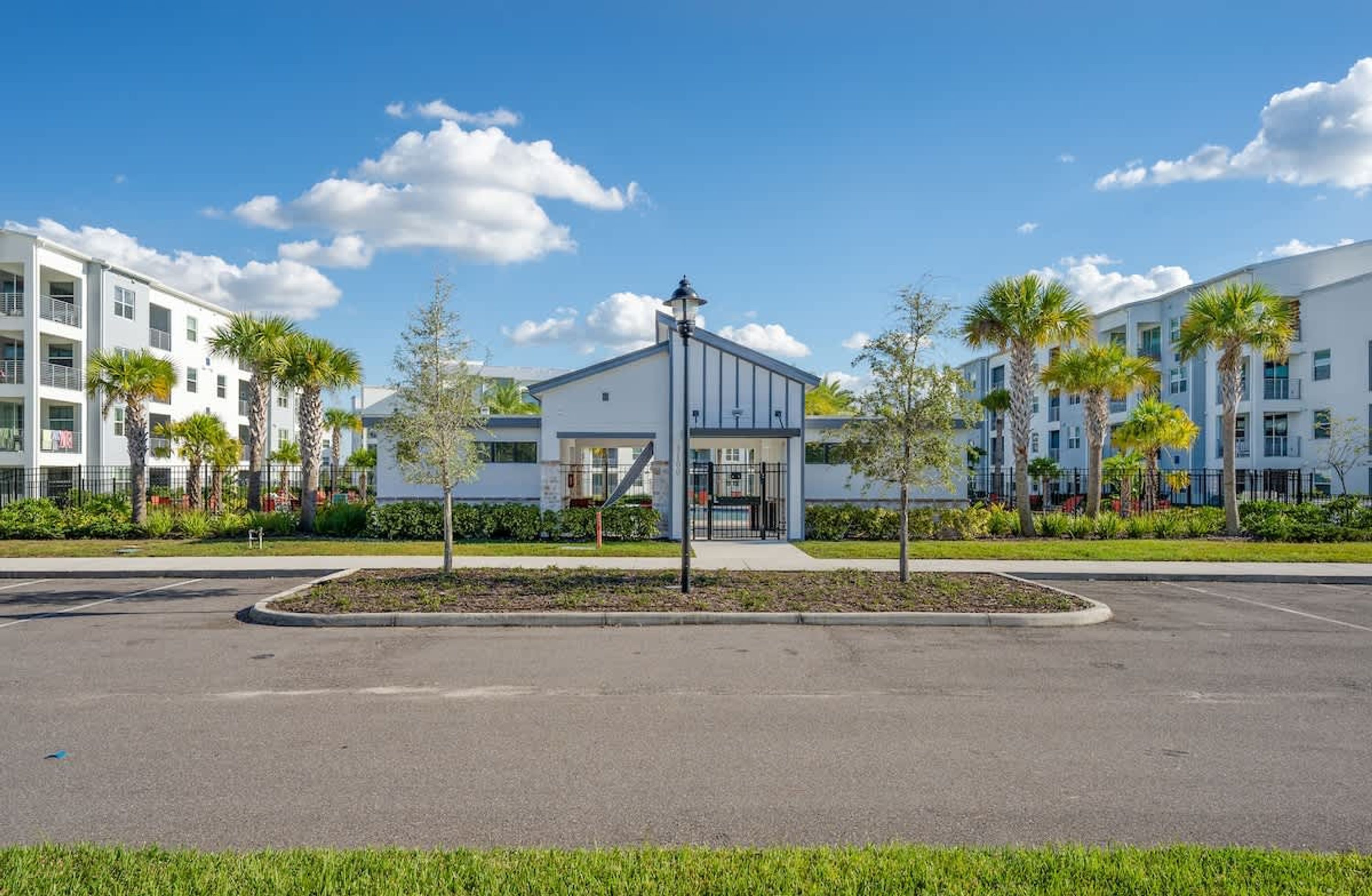 A modern building with a central entrance, surrounded by a landscaped area with palm trees and a parking lot.