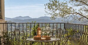 A balcony with a table set for two, featuring a bottle and glasses, overlooking a mountainous landscape.