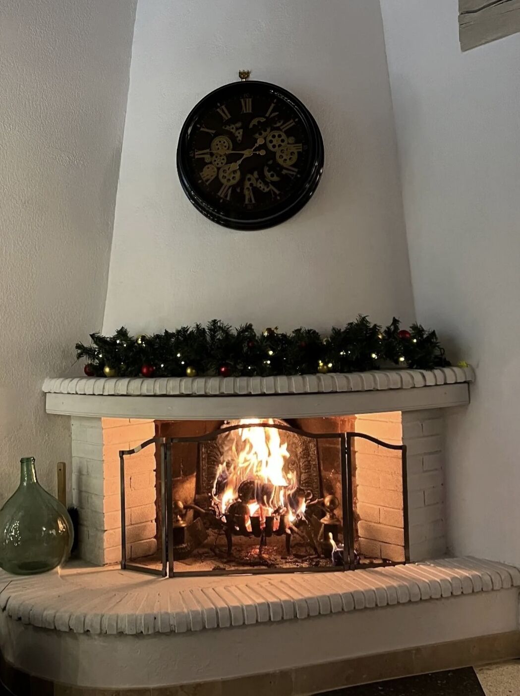 Una chimenea con un reloj encima, un fuste de ladrillo y un árbol de Navidad con luces.