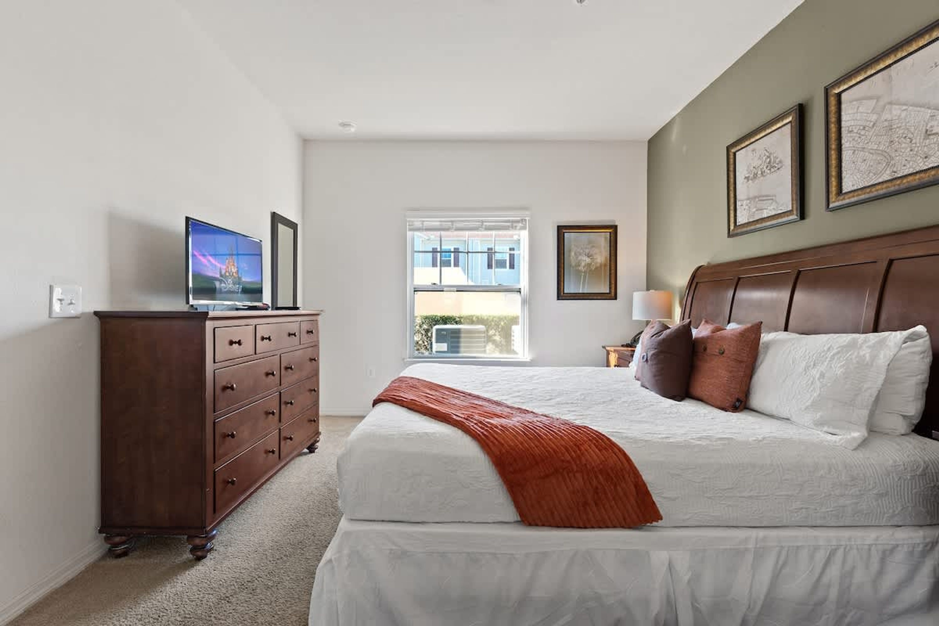 Une chambre à coucher avec un lit, une commode, une télévision et des œuvres d’art accrochées au mur.
