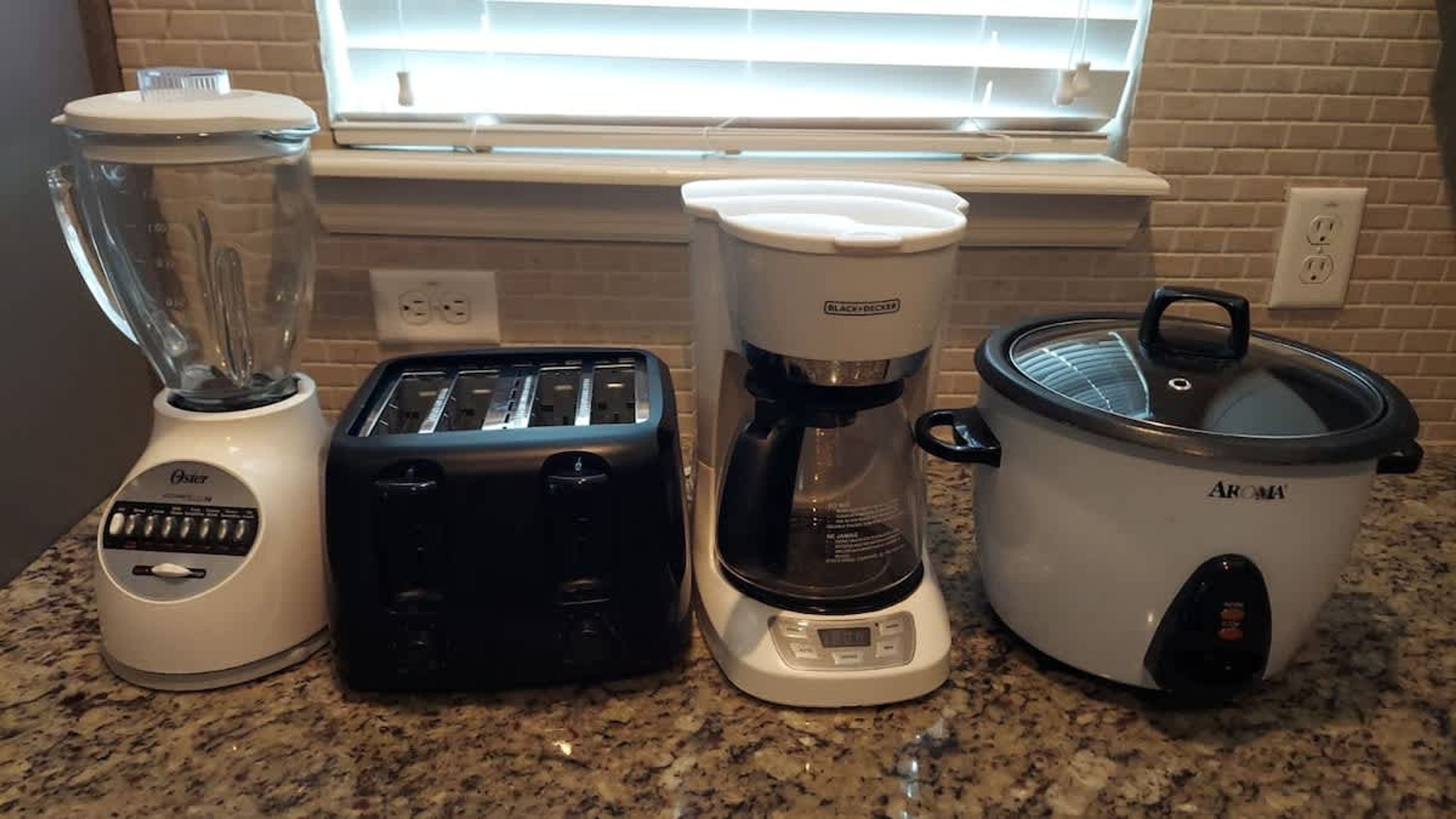 Uma bancada de cozinha com liquidificador, torradeira, cafeteira e cozido lento.