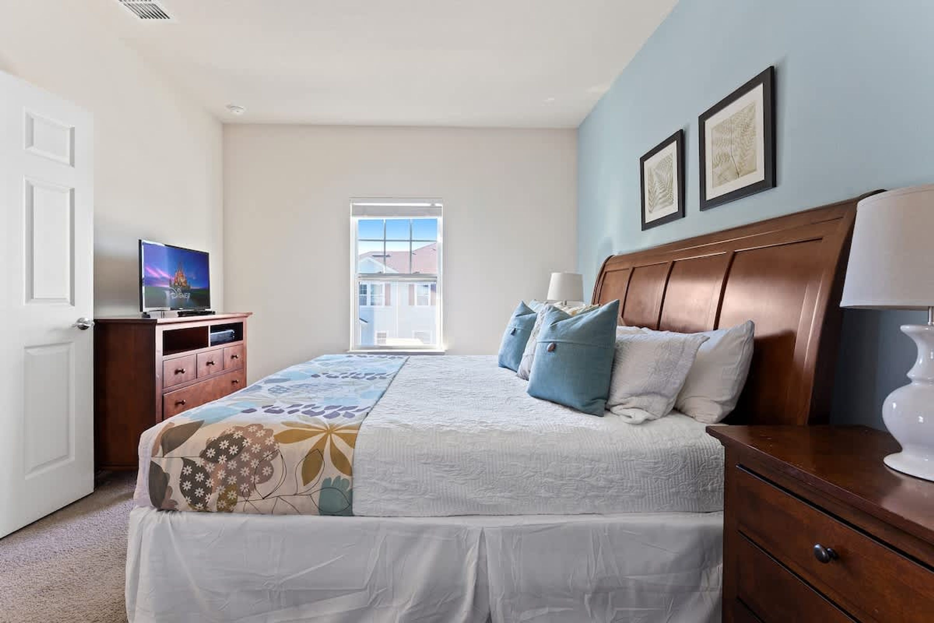 Une chambre à coucher comprenant un lit, une commode, un téléviseur et une fenêtre donnant sur des immeubles.