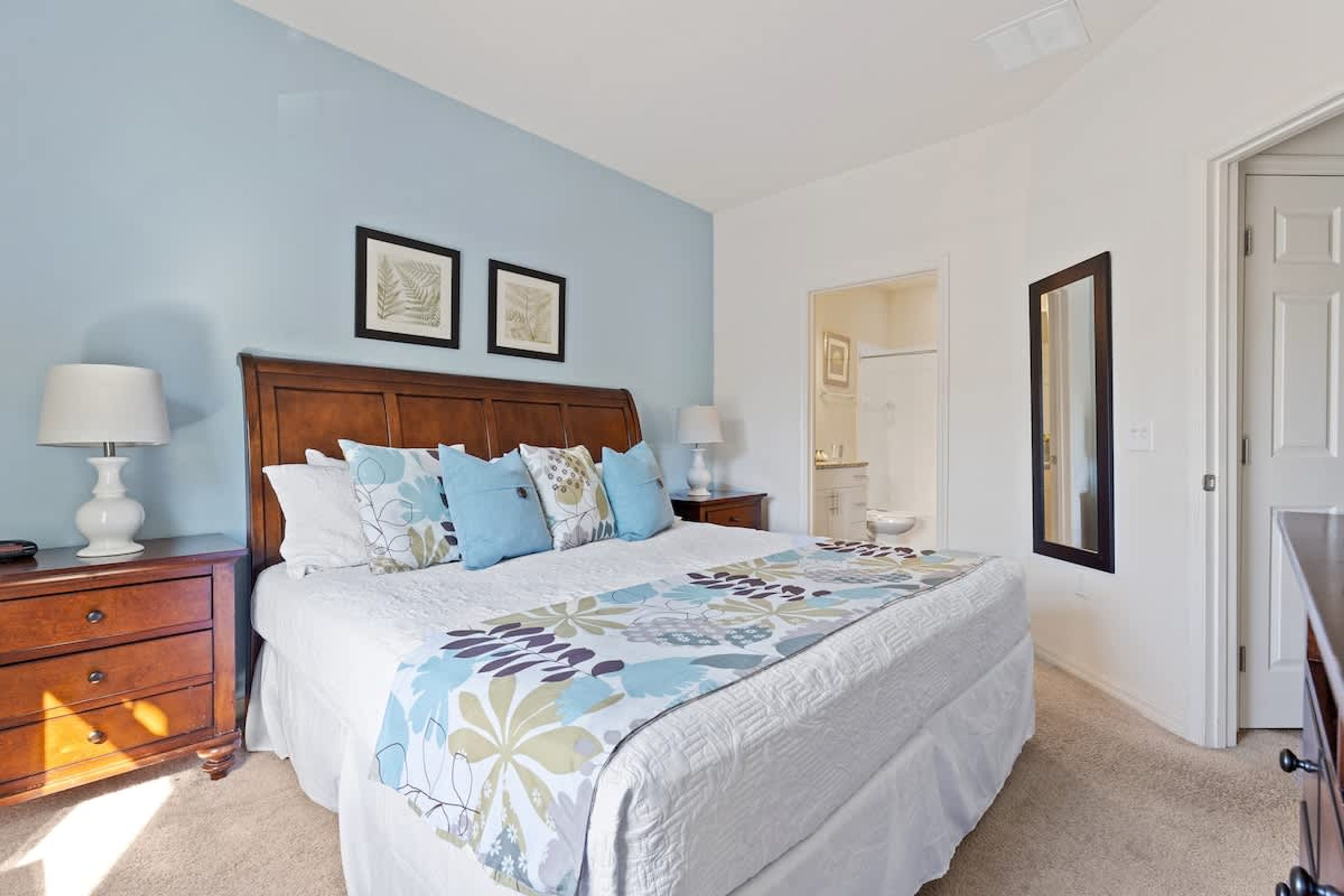 A bedroom with a large bed, two bedside tables, a nightstand, a mirror, and a door.