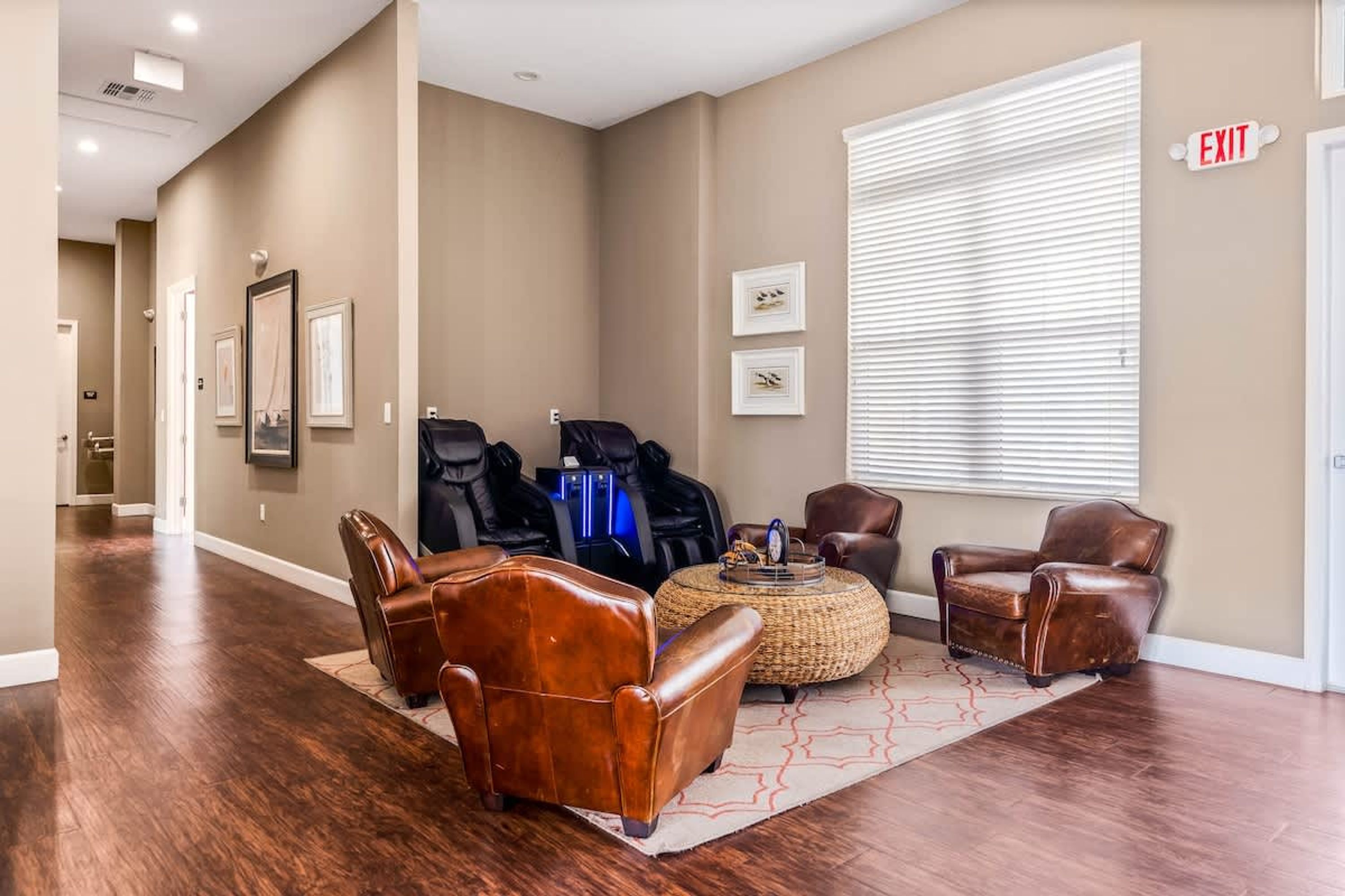 A lobby with leather chairs, massage chairs, and a large window with blinds.