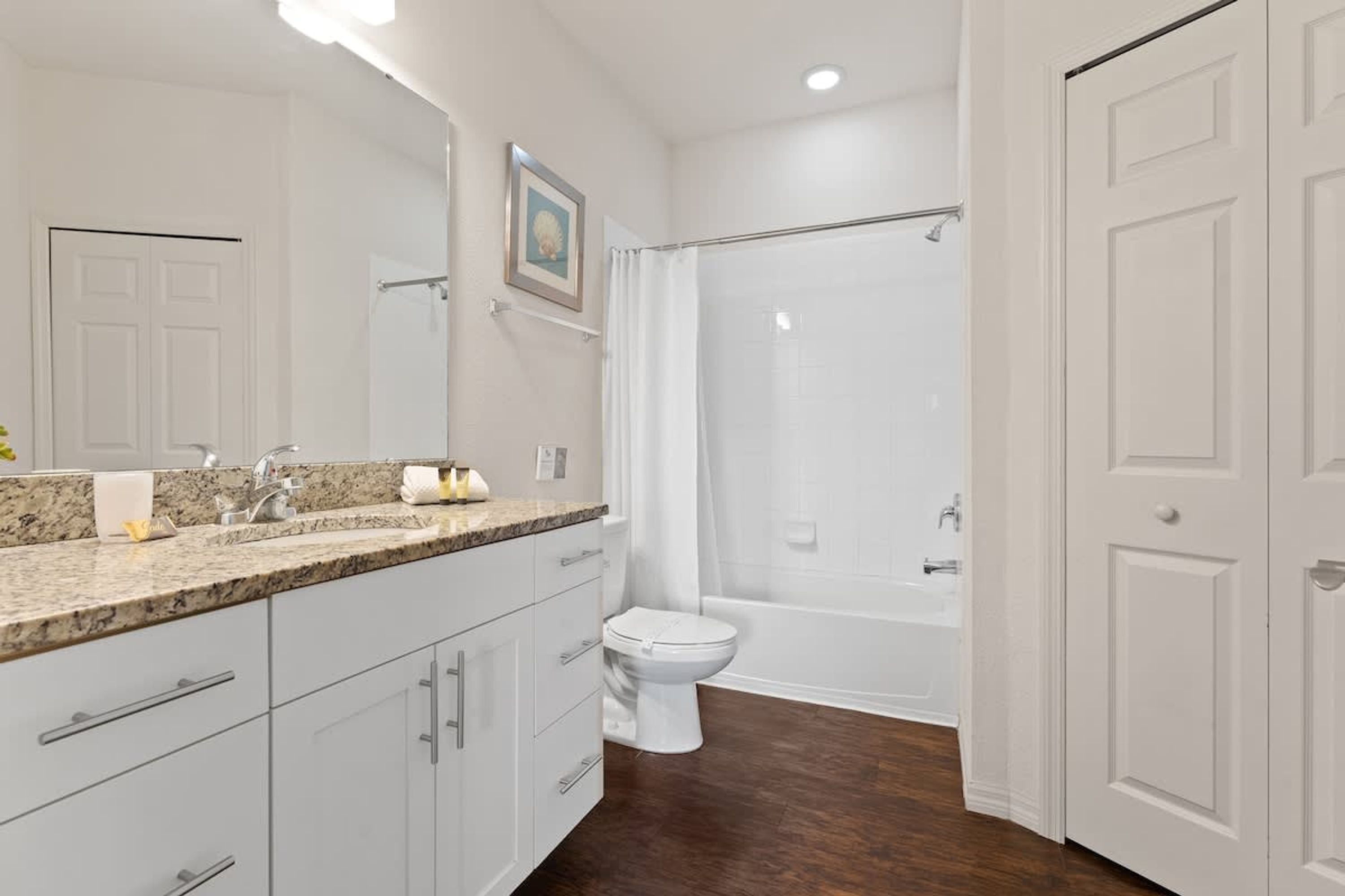 A modern bathroom with a granite countertop sink, a white toilet, a bathtub, and a shower curtain.