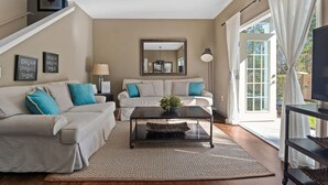 A living room with a sofa, coffee table, and a TV stand. There is a staircase on the left and a large window on the right. - Charming Townhouse 4 BR up to 12 People Wl8972 (Kissimmee)