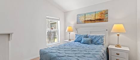 A bedroom with a large bed, two bedside tables with lamps, a window, and a painting on the wall.