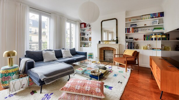 Un salon avec un canapé, une table basse et une cheminée. On y trouve également des étagères et un miroir au mur.