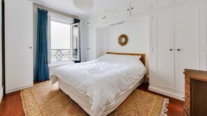 Une chambre à coucher avec un lit, une commode, une armoire et une fenêtre avec des rideaux.