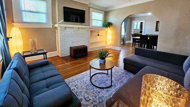 A modern living room with a fireplace, sofas, a TV, and a dining area. - Charming House in Midtown Memphis near Beale St and St Jude  (Memphis)