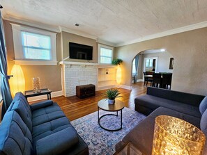 A modern living room with a fireplace, sofas, a TV, and a dining area. - Charming House in Midtown Memphis near Beale St and St Jude  (Memphis)