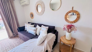 A modern living room with a dark sofa, multiple cushions, a small wooden side table with a vase of flowers, and three wall-mounted mirrors. - MAR SOL Villa in Vilamoura (Loulé)
